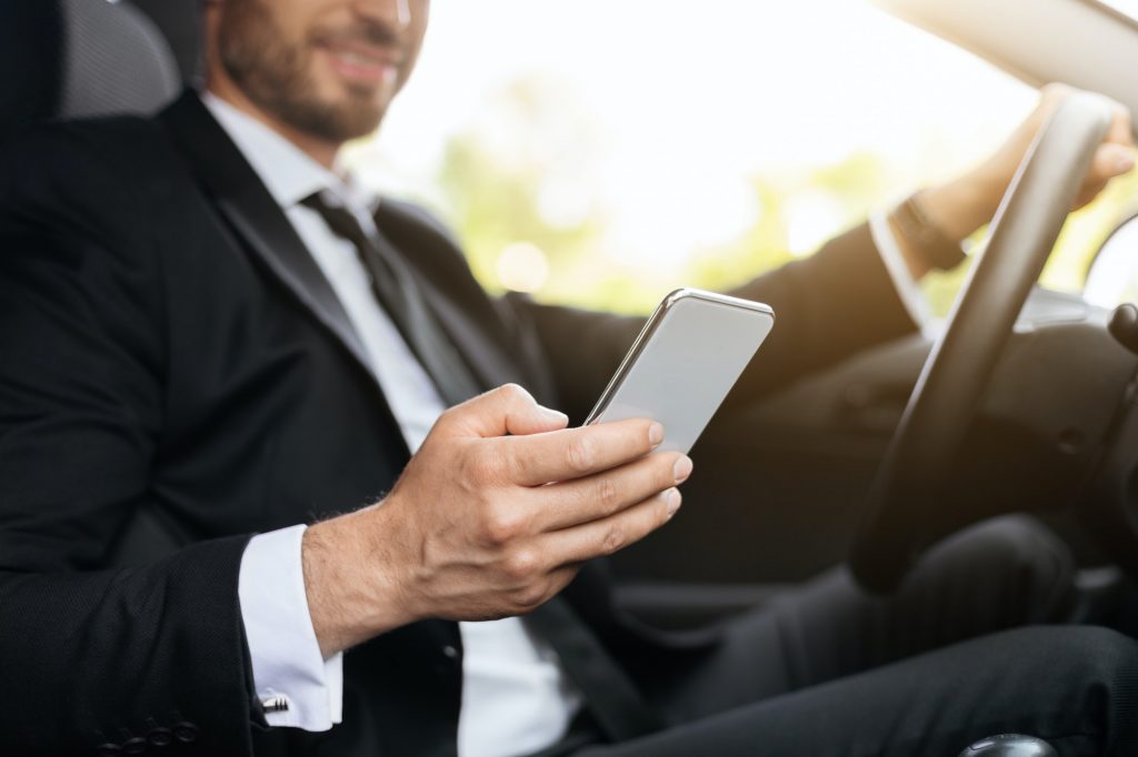 Cropped of businessman driving car, using mobile phone